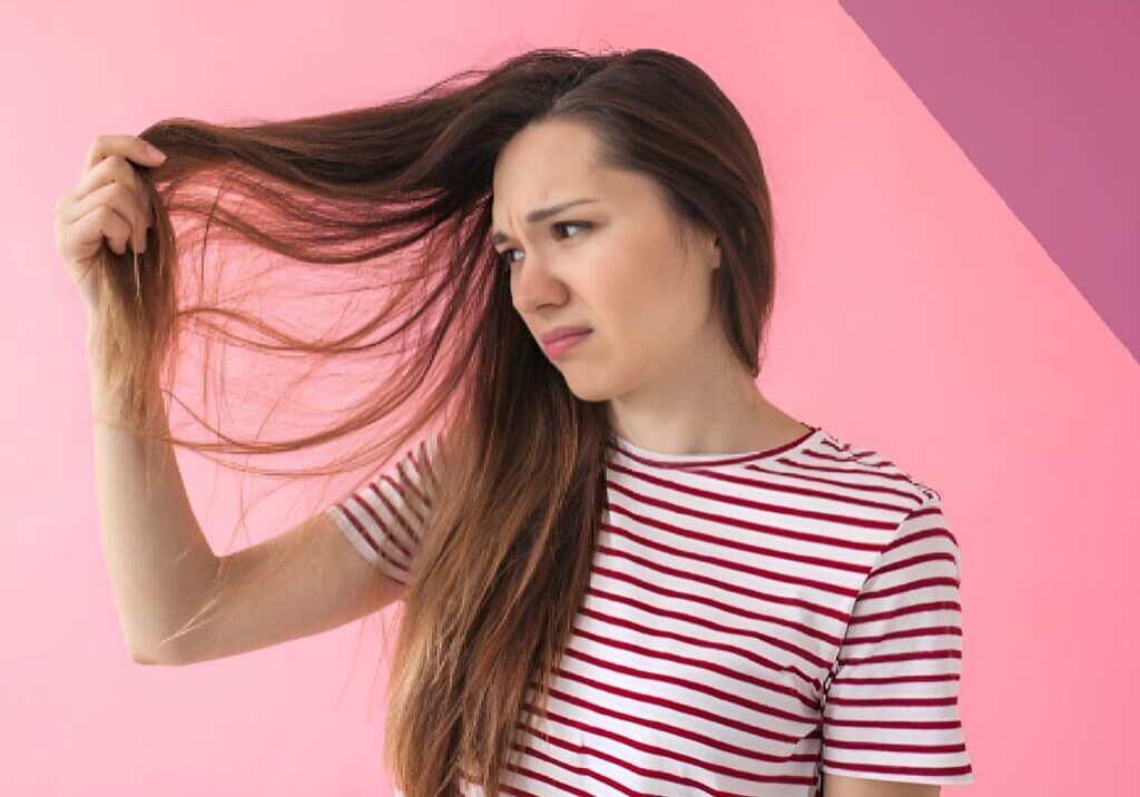 A woman with long hair is standing against a pink wall.