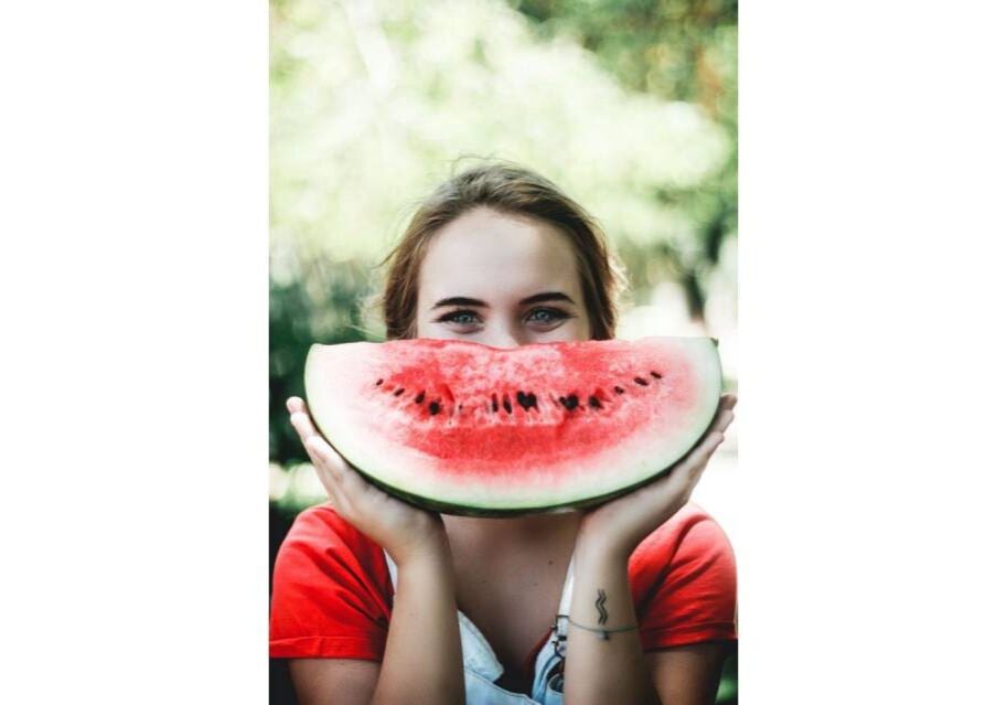 A woman holding up a slice of watermelon to her face.