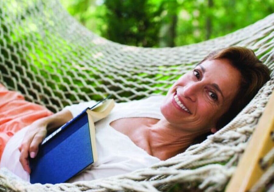 A woman laying in a hammock with her head resting on the edge of a book.
