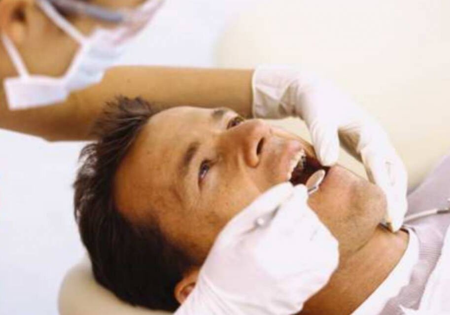 A man getting his teeth brushed by another person.