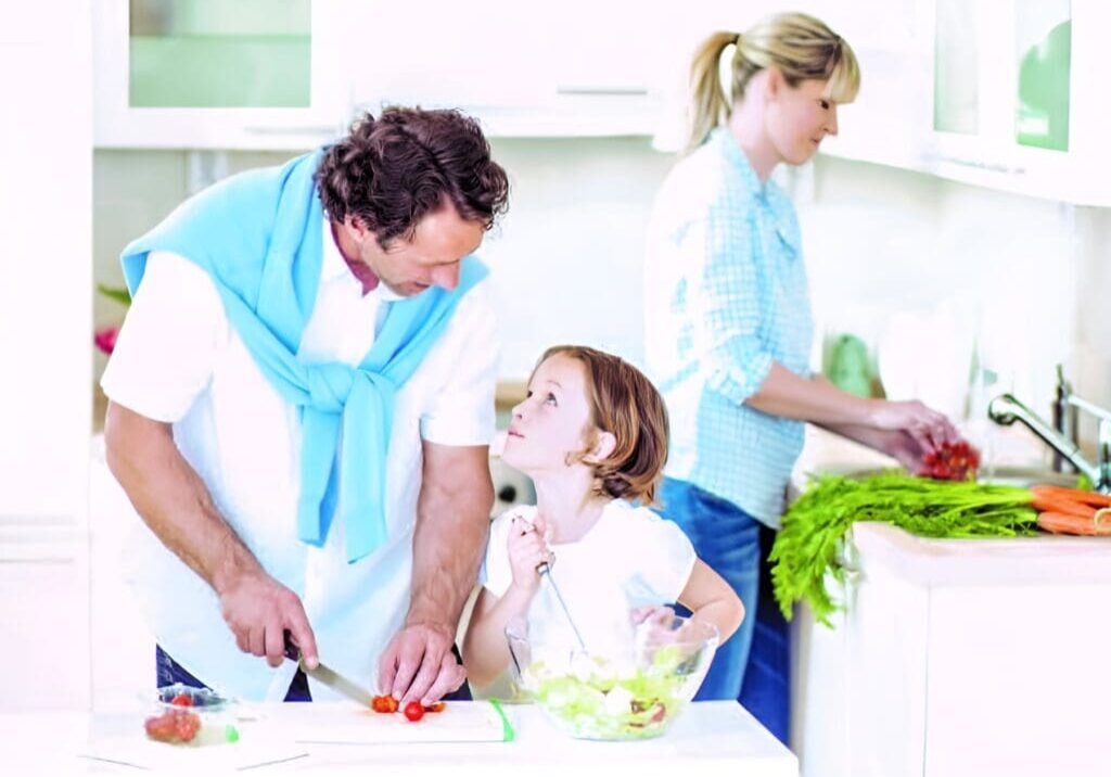 A man and woman helping a child cut vegetables.