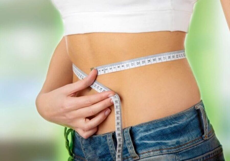 A woman is measuring her waist with a tape measure.