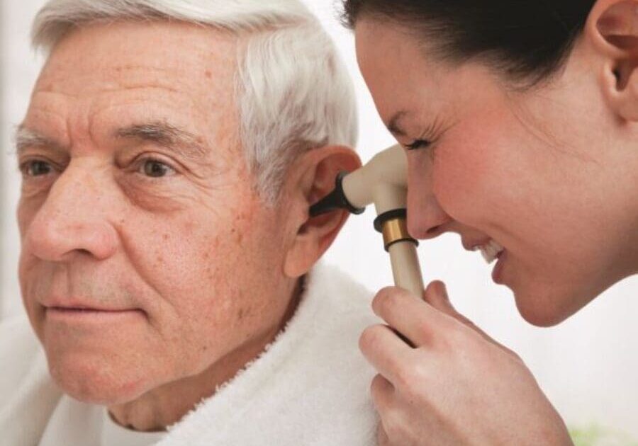 A woman is putting an ear piece on the ear of an older man.