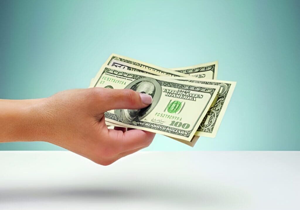 A person holding two hundred dollar bills in their hand.
