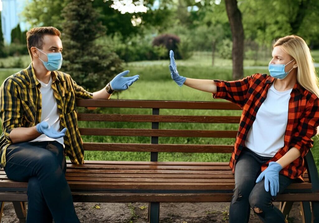 Two people wearing masks and gloves on a bench.